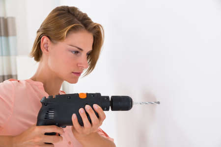 Portrait Of Young Woman Making Hole In Wall With Drill Machineの写真素材