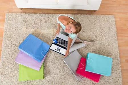 High Angle View Of Young Woman With Shopping Bags Using Laptop For Online Shoppingの写真素材