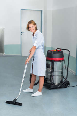 Young Female Cleaner In Uniform Vacuuming Floorの写真素材