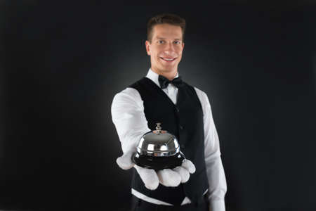 Portrait Of Happy Waiter Holding Service Bell In Handsの写真素材