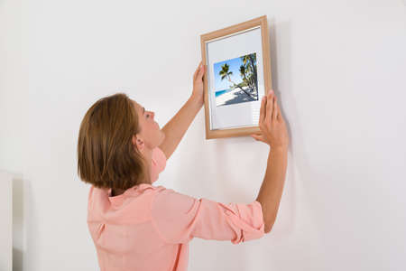 Young Woman Putting Photo Frame On White Wallの写真素材