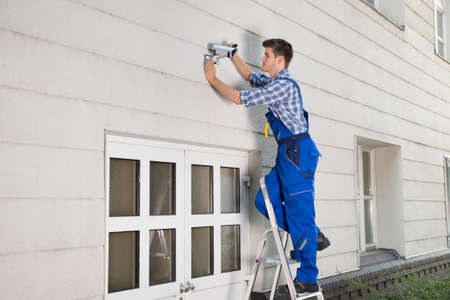 Young Happy Male Technician Fixing Cctv Camera On Wallの写真素材