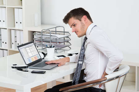 Young Businessman Suffering From Backpain While Working On Laptop In Office