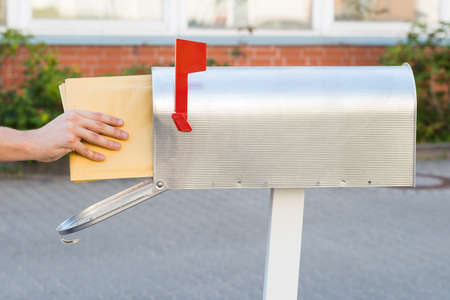 Close-up Of Person Putting Stack Of Letters In Mailboxの写真素材