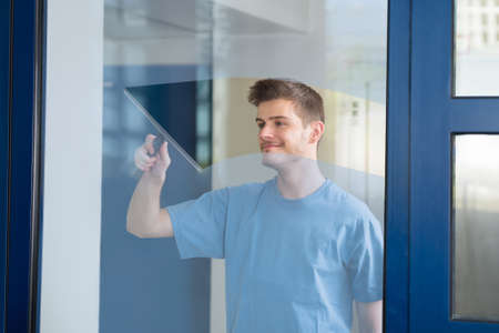 Young Male Worker Cleaning Glass With Squeegeeの写真素材