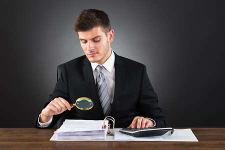 Young Businessman Scrutinizing Invoice With Magnifying Glassの写真素材