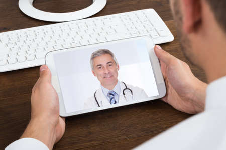 Close-up Of Businessperson Videochatting With Senior Doctor On Mobile Phoneの写真素材