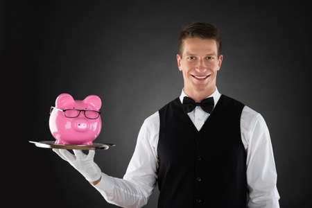Portrait Of Happy Butler Holding Tray With Pink Piggybankの写真素材