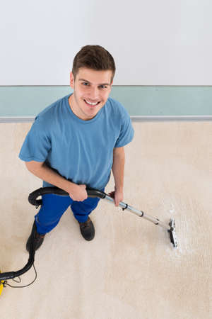 High Angle View Of Young Happy Male Janitor Vacuuming Corridor Officeの写真素材