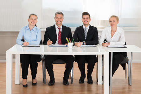 Group Of Happy Businesspeople Analyzing Graph At Desk