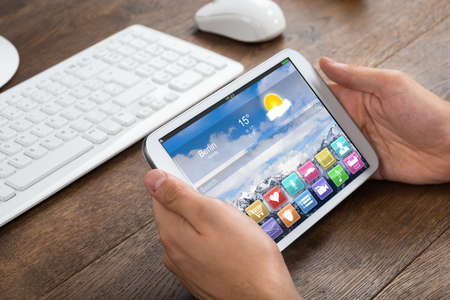 Close-up Of Businessperson Holding Mobile Phone With Apps At Desk
