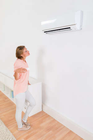 Young Woman Operating Air Conditioner With Remote Control