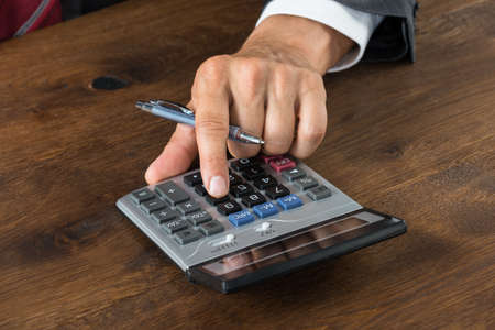 Cropped image of businessman using calculator at wooden deskの写真素材