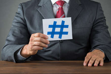 Midsection of businessman showing hash sign on paper at deskの写真素材