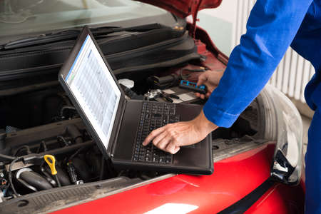 High Angle View Of Mechanic Examining Car Engine With Help Of Laptopの写真素材