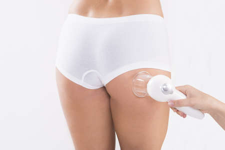 Midsection of young woman receiving cellulite vacuum therapy on buttock over white backgroundの写真素材