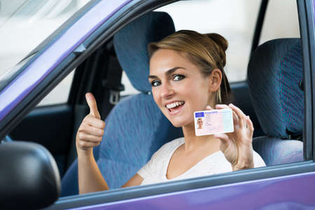 Portrait of excited young woman showing license while sitting in car