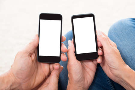 Close-up Of Two People Hands Holding Blank Display Mobile Phonesの写真素材