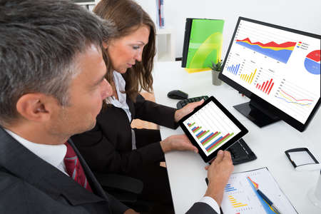 Two Businesspeople Analyzing Graph On Digital Tablet In Office