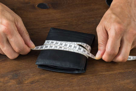 Cropped image of businessman wrapping wallet with tape measure at deskの写真素材