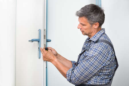 Male carpenter fixing lock in door with screwdriver at homeの写真素材