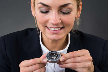 Closeup of young businesswoman holding compass over gray backgroundの写真素材