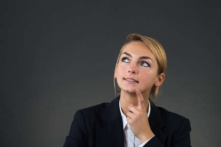 Thoughtful young businesswoman looking up over gray backgroundの写真素材