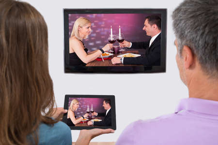 Rear View Of Couple Connecting Television Channel Through Wifi On Digital Tablet