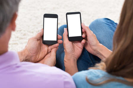 Close-up Of Mature Couple Holding Mobile Phones With Blank Screenの写真素材