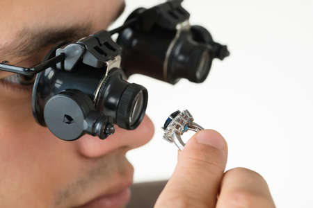 Closeup of jeweler examining diamond ring with magnifying loupe against white background