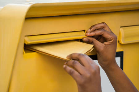 Close-up Of A Person's Hand Inserting Letter In Mailboxの写真素材