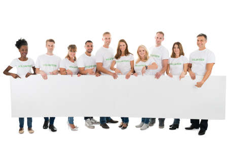 Full length portrait of confident volunteers holding blank billboard against white backgroundの写真素材