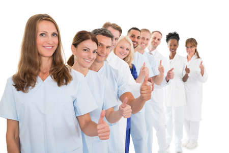Portrait of confident medical team showing thumbs up while standing in line against white background