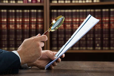 Cropped image of lawyer examining documents with magnifying glass in courtroomの写真素材