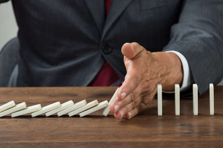 Midsection of businessman stopping dominoes falling on wooden desk