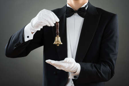 Midsection of waiter holding ring bell while standing against gray backgroundの写真素材