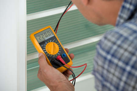 Cropped image of male repairman checking fridge with digital multimeter at homeの写真素材