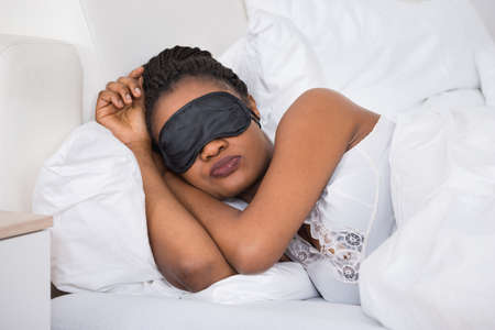 African Woman Wearing Eyemask While Sleeping On Bedの写真素材