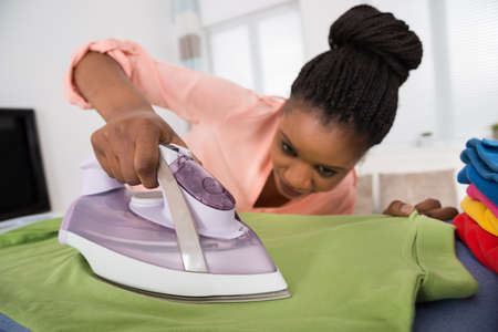 Young African Woman Ironing Clothes With Steam Ironの写真素材