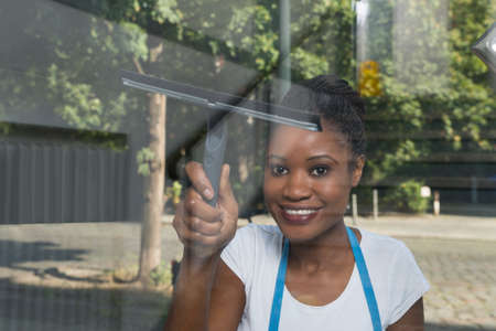 African Woman Cleaning Glass With Rubber Window Cleaner From Outsideの写真素材