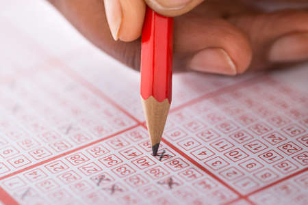 Close-up Of Person's Hand Marking Number On Lottery Ticket With Pencilの写真素材
