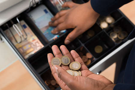 Close-up Of Person's Hand Holding Euro Note Over Container