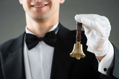 Midsection of waiter holding ring bell against gray backgroundの写真素材