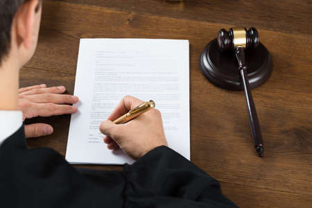 High angle view of male judge writing on legal documents at desk in courtroomの写真素材
