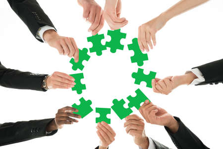 Directly below shot of business team joining jigsaw pieces in huddle against white backgroundの写真素材