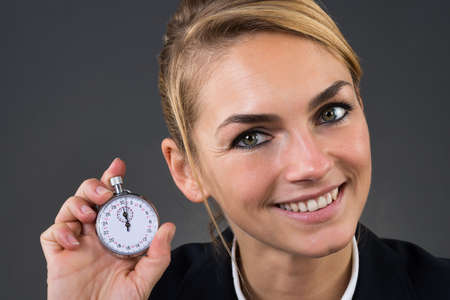 Closeup of young businesswoman showing stopwatch over gray backgroundの写真素材
