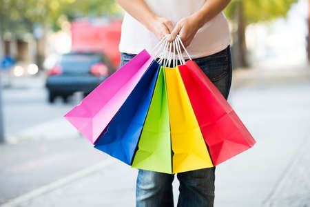 Midsection of young woman holding colorful shopping bags