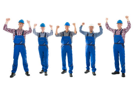 Full length portrait of successful carpenters with arms raised standing in row against white backgroundの写真素材
