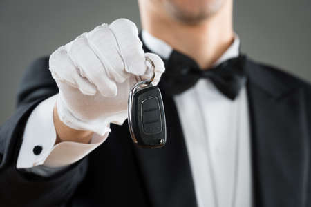 Midsection of waiter holding car key against gray background