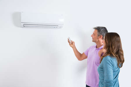 Mature Couple Standing In Front Of Air Conditioner And Adjusting The Temperature By Remoteの写真素材